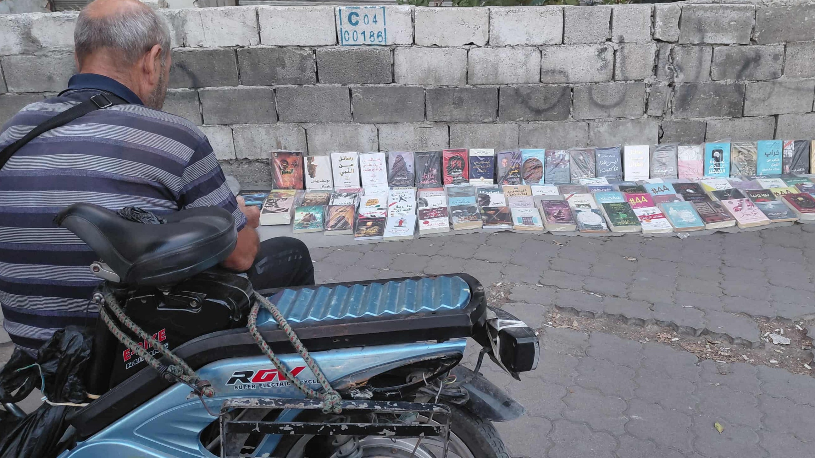 Uncle Abu Mohammed.. Stini sells books on the sidewalk to fight hunger, sun, and law!